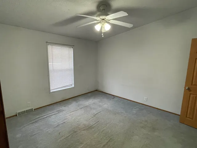 an empty room with a chandelier fan and windows