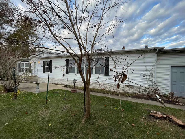 a view of a white house in front of a big yard plants and large trees