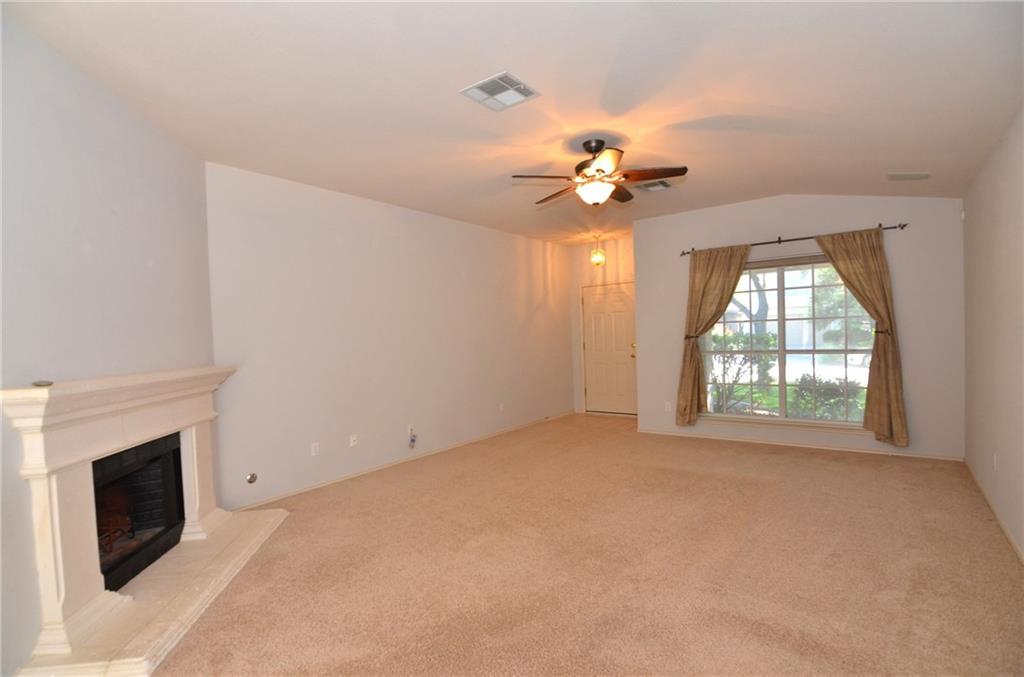 3609 Ruby Red Drive Austin, TX 78728 - Photo 4 of 21 Unfurnished living room featuring ceiling fan, a fireplace with raised hearth, and light carpet