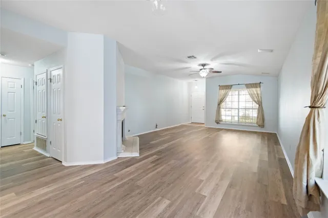 an empty room with wooden floor fan and windows
