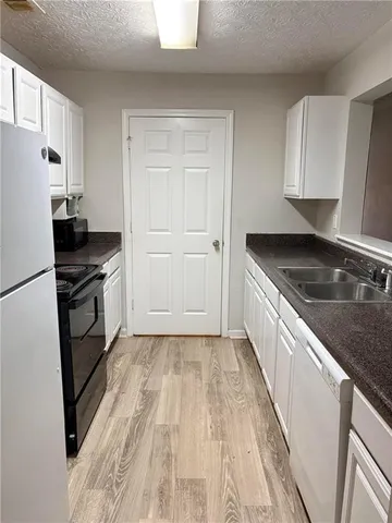 a kitchen with granite countertop a refrigerator a sink and white cabinets