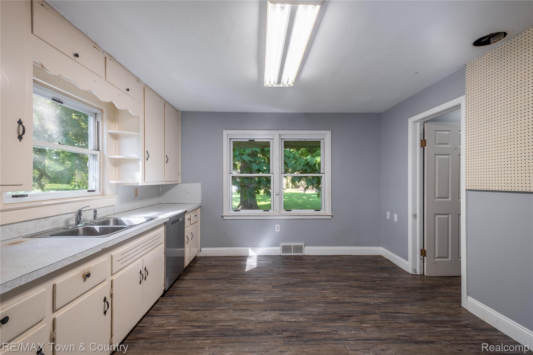 300 Elms Road Flushing, MI 48433 - Photo 6 of 26 Kitchen featuring wood-finish flooring, two large windows, extensive cabinetry, double basin sink, and a dishwasher
