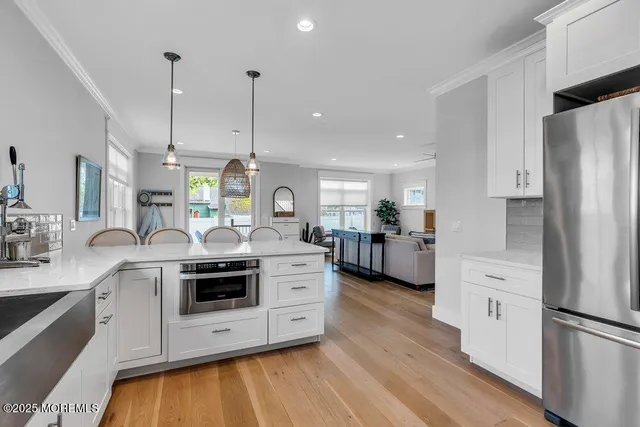 a kitchen with stainless steel appliances a stove a sink dishwasher a refrigerator and white cabinets with wooden floor