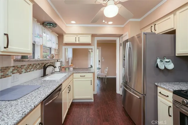 a kitchen with granite countertop a refrigerator a sink dishwasher a stove and white cabinets with wooden floor