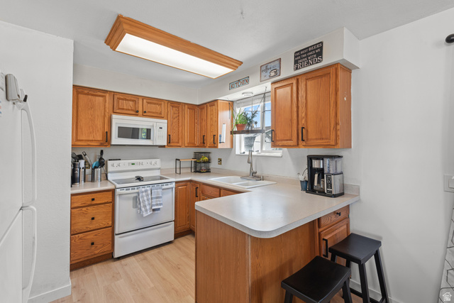 3951 Brixton Road Salt Lake City, UT 84129 - Photo 11 of 22 Kitchen featuring light wood-finish cabinetry, white appliances, light countertops, a double basin sink, and wood-finish flooring