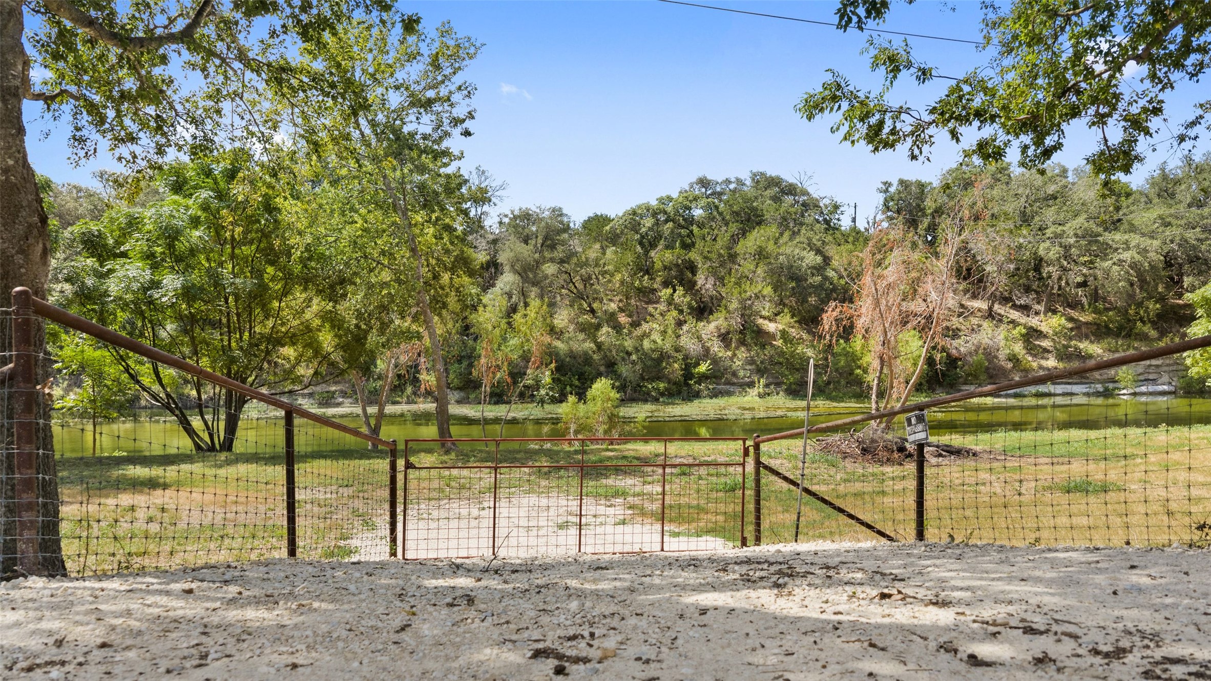 3764 Ranch Road 1623 Blanco, TX 78606 - Photo 7 of 36 Mature trees frame a peaceful waterfront view framed by wire fencing.