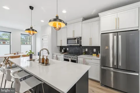 a kitchen with stainless steel appliances granite countertop a sink a stove a refrigerator a center island a dining table and chairs
