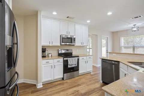 a kitchen with stainless steel appliances granite countertop a refrigerator a sink dishwasher a stove and white countertops with wooden floor