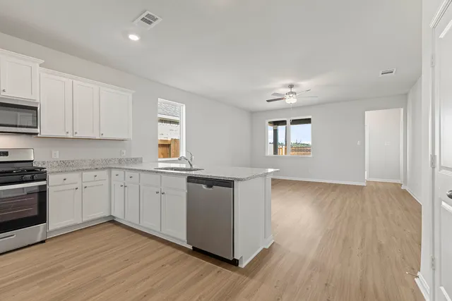 a kitchen with stainless steel appliances granite countertop a stove top oven a sink dishwasher and white cabinets with wooden floor