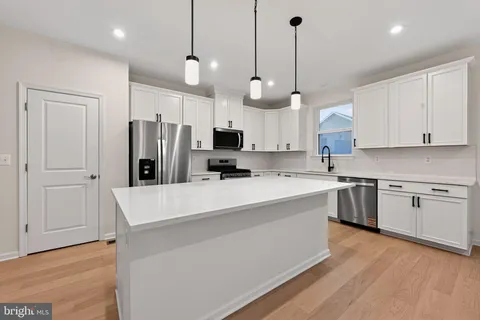 a large kitchen with stainless steel appliances kitchen island granite countertop a stove a sink a refrigerator and white cabinets with wooden floor