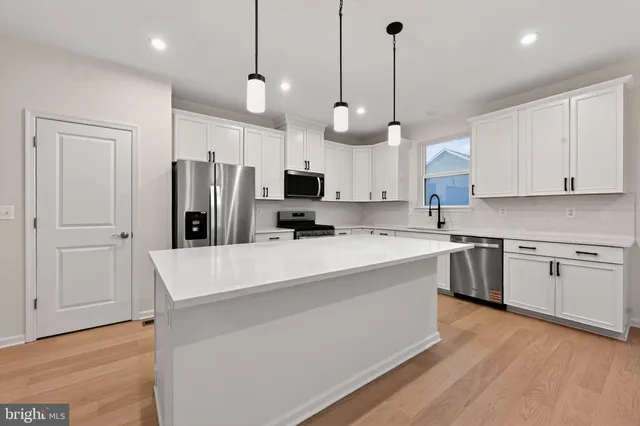a large kitchen with stainless steel appliances kitchen island granite countertop a stove a sink a refrigerator and white cabinets with wooden floor