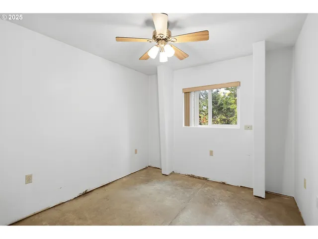a view of an empty room and window with chandelier fan