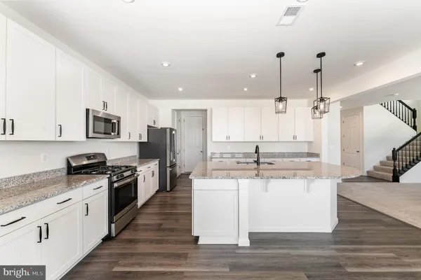 a kitchen with stainless steel appliances granite countertop a sink a stove a refrigerator and white cabinets