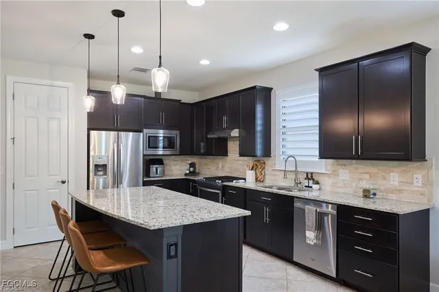 a kitchen with granite countertop stainless steel appliances a sink a stove a refrigerator a center island and cabinets