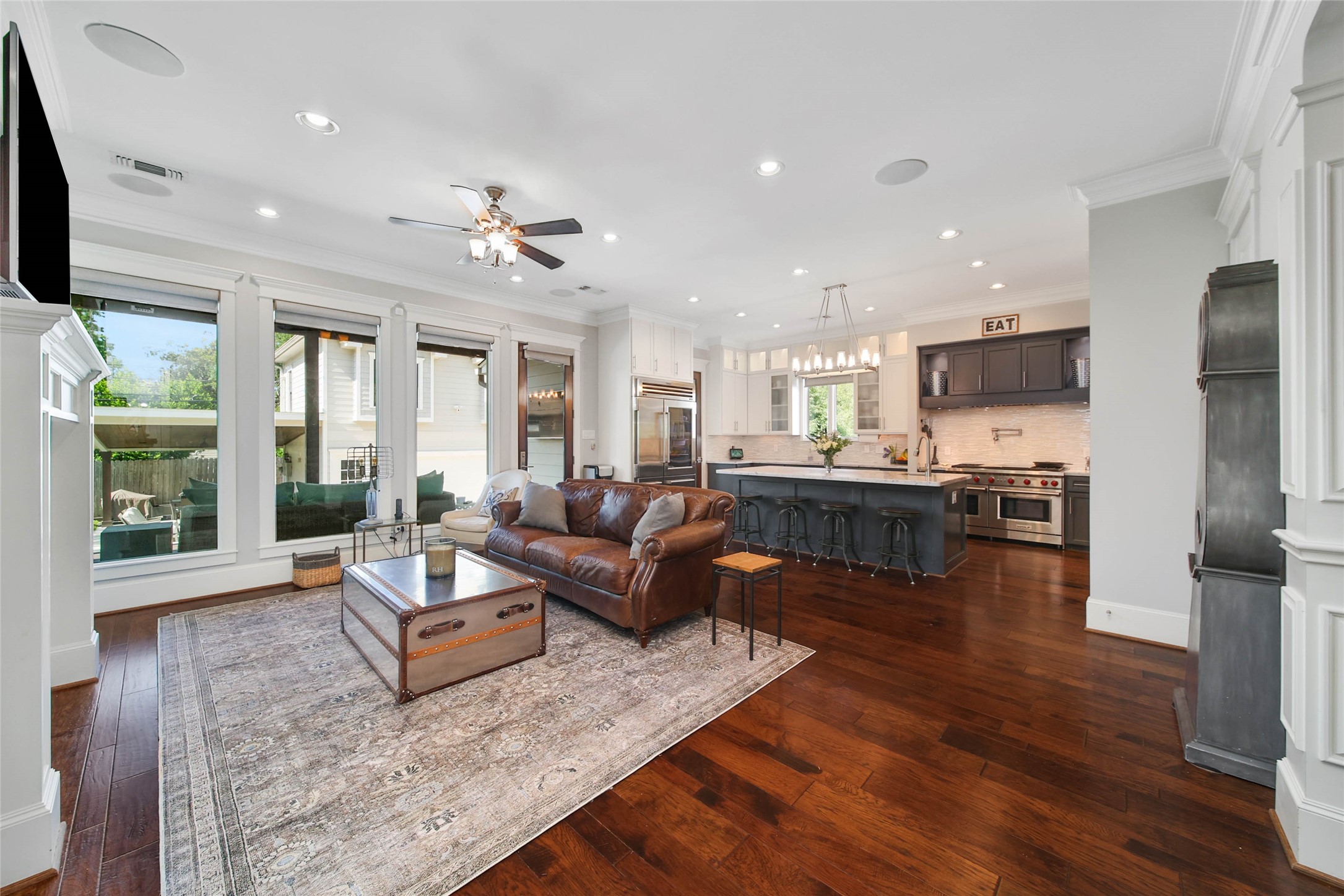 416 West 33rd Street Houston, TX 77018 - Photo 10 of 47 Stunning open-concept living and entertaining space showcasing rich hardwood floors, extensive crown molding, integrated in-ceiling speaker system and walls of oversized windows that flood the home with natural light. The designer kitchen is beautifully appointed with premium stainless appliances, custom cabinetry and an oversized island with bar seating, all seamlessly connected to the sophisticated family room and outdoor living spaces beyond.