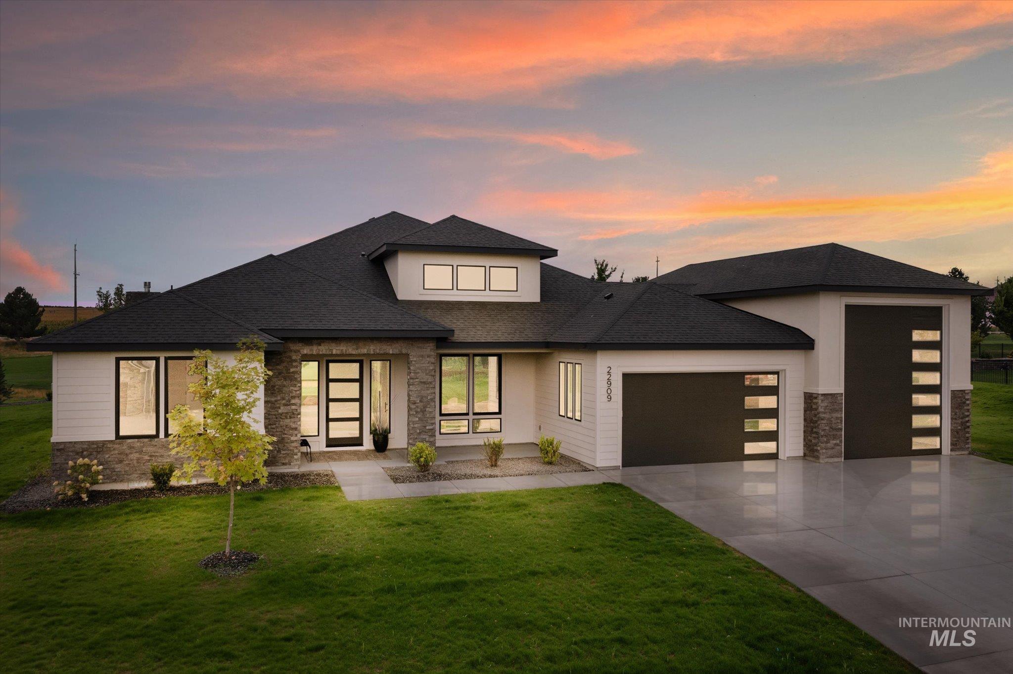 Prairie-style house with stone siding, an attached garage, roof with shingles, concrete driveway, and a yard