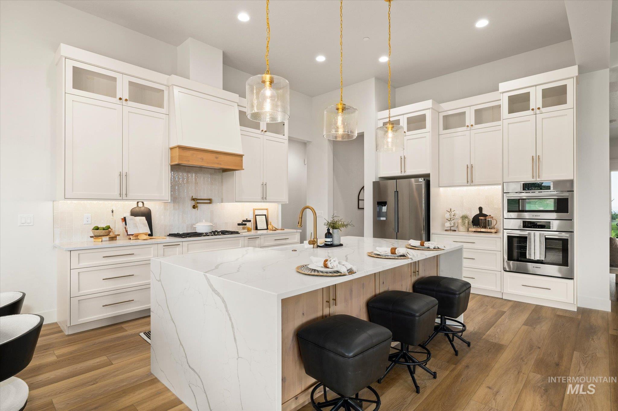 22909 Cirrus Vw Court Caldwell, ID 83607 - Photo 13 of 50 Kitchen featuring glass insert cabinets, decorative backsplash, light stone counters, pendant lighting, and a breakfast bar