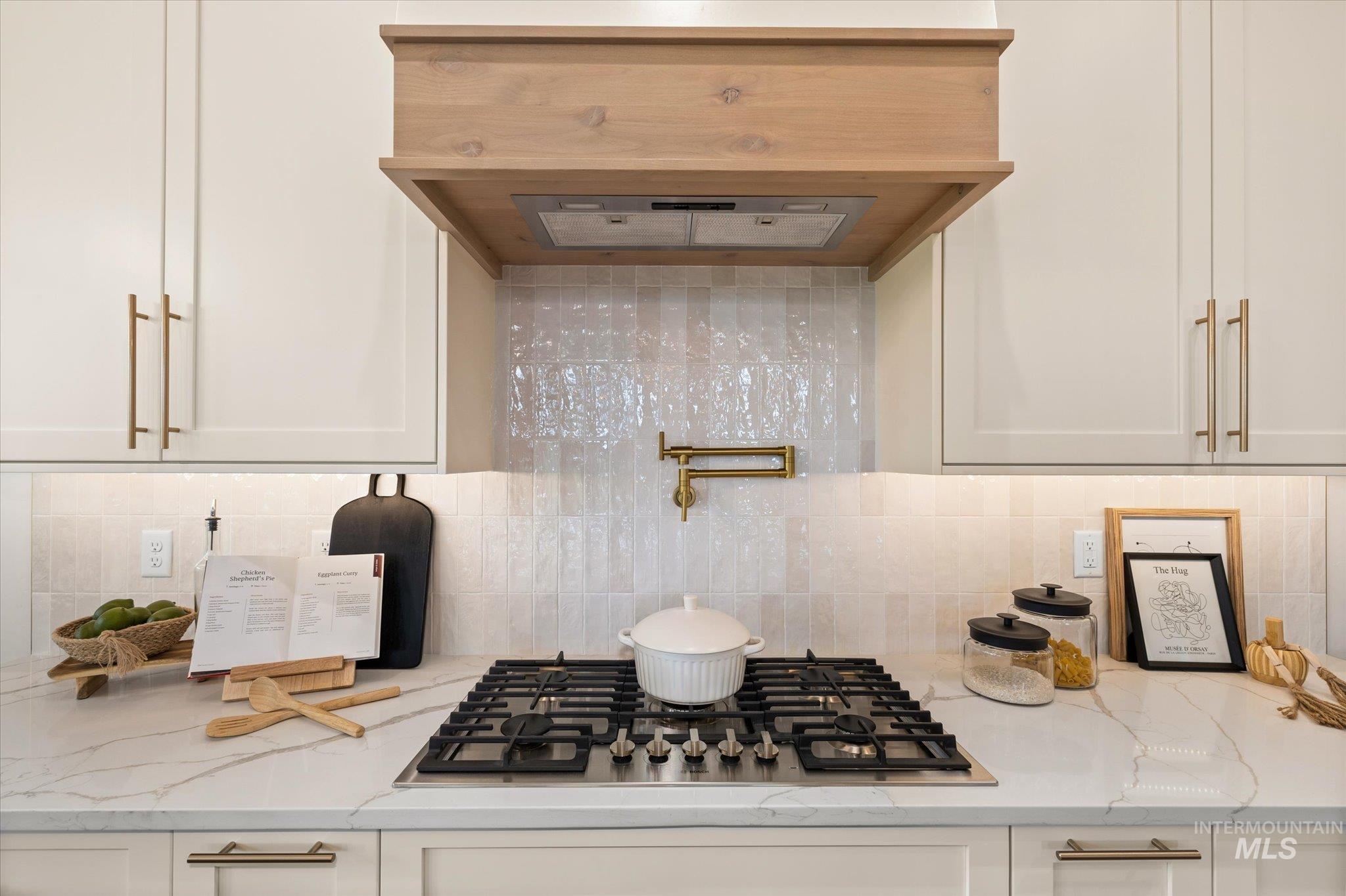 22909 Cirrus Vw Court Caldwell, ID 83607 - Photo 15 of 50 Kitchen featuring exhaust hood, tasteful backsplash, light stone countertops, stainless steel gas stovetop, and white cabinetry