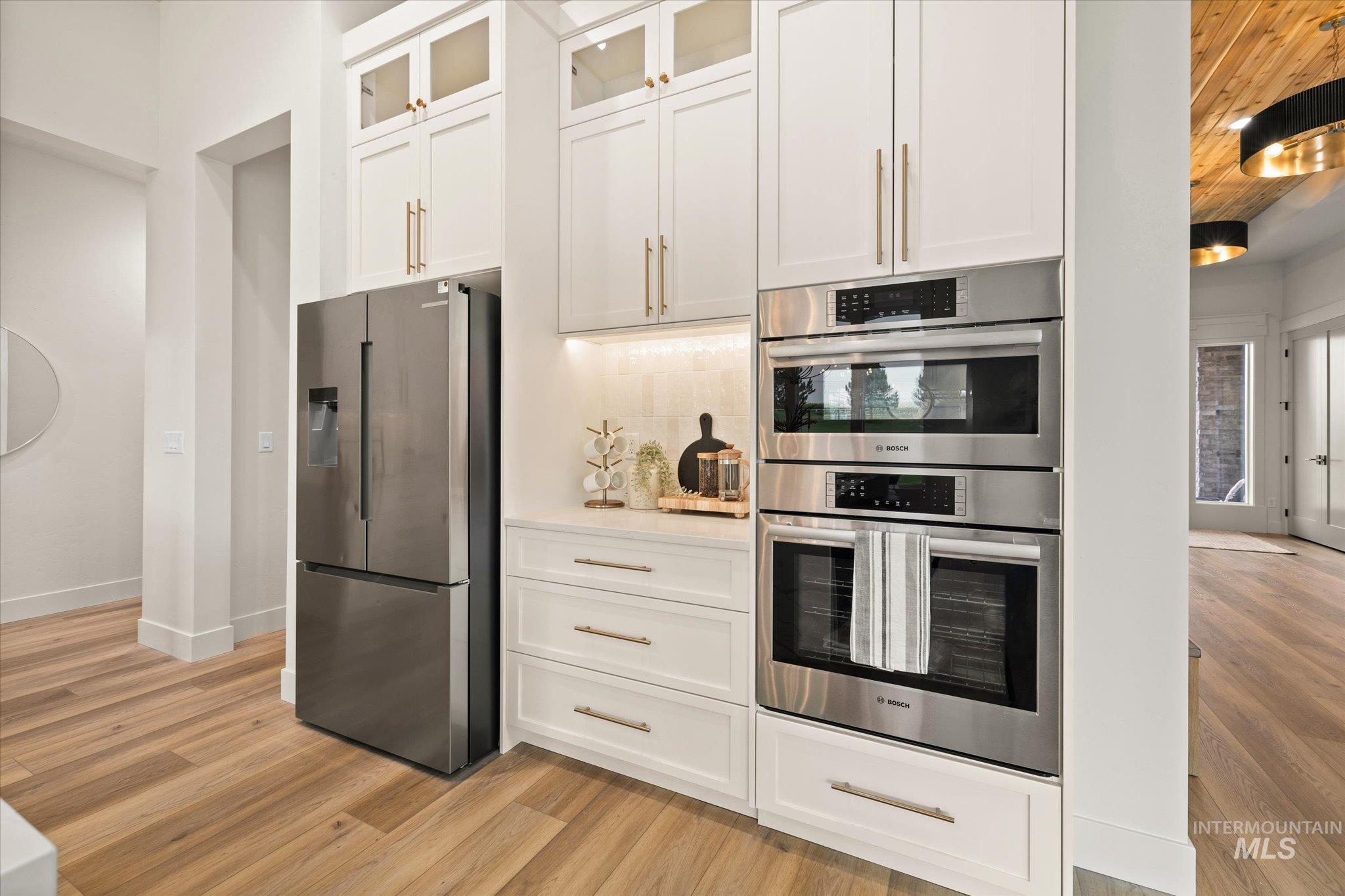 22909 Cirrus Vw Court Caldwell, ID 83607 - Photo 17 of 50 Kitchen with stainless steel appliances, white cabinetry, glass insert cabinets, light wood-style flooring, and decorative backsplash