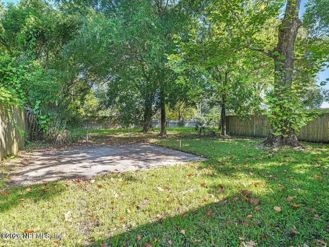 a view of a backyard with large trees and wooden fence