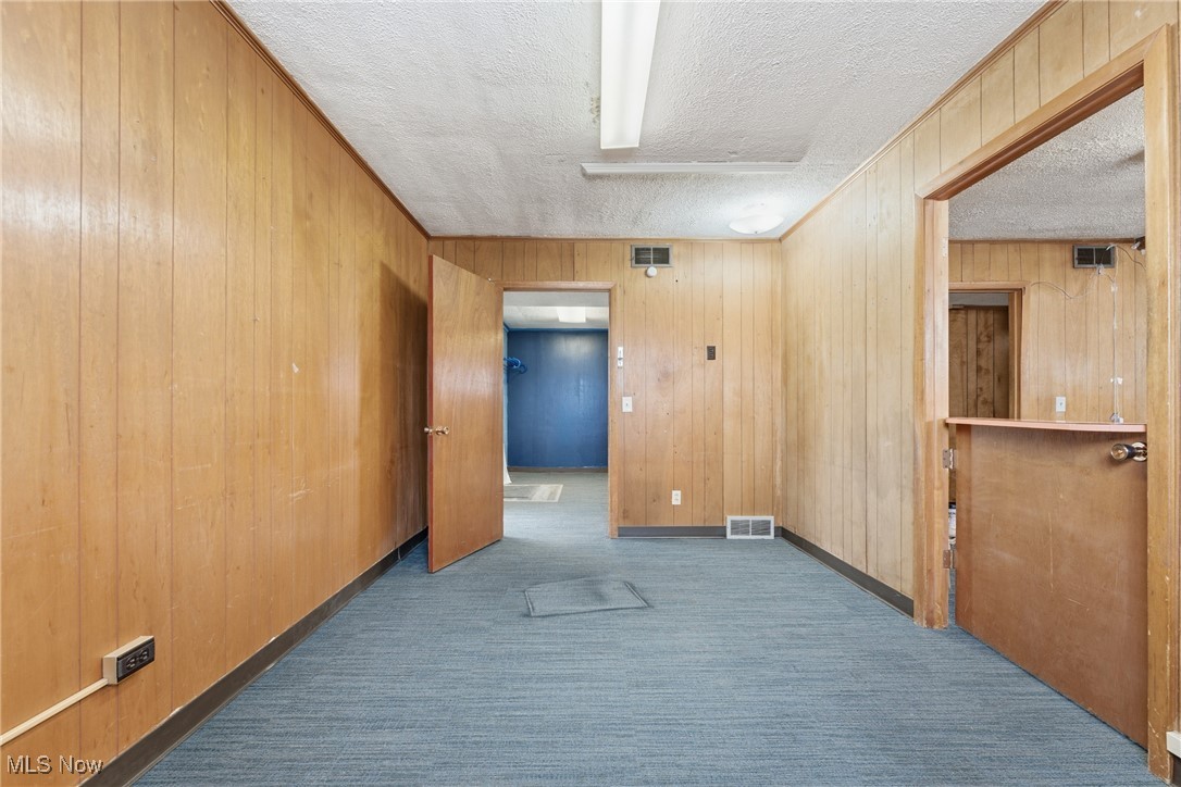 1817 Fulton Road Northwest Canton, OH 44709 - Photo 7 of 25 Unfurnished room with dark carpet, wood walls, and a textured ceiling
