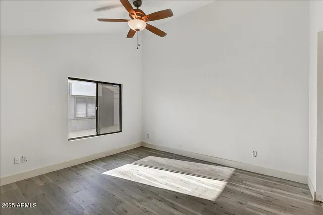 an empty room with wooden floor fan and windows