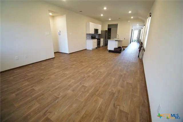 an empty room with wooden floor and kitchen view