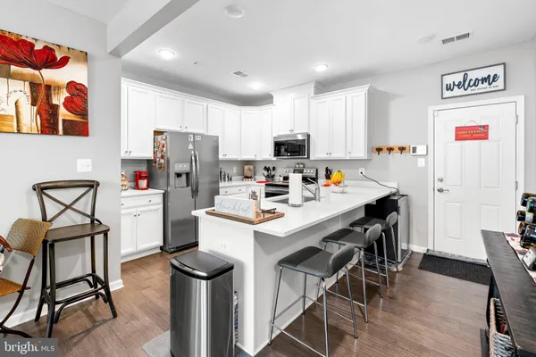 a kitchen with stainless steel appliances a stove a refrigerator a sink a dining table and chairs with wooden floor