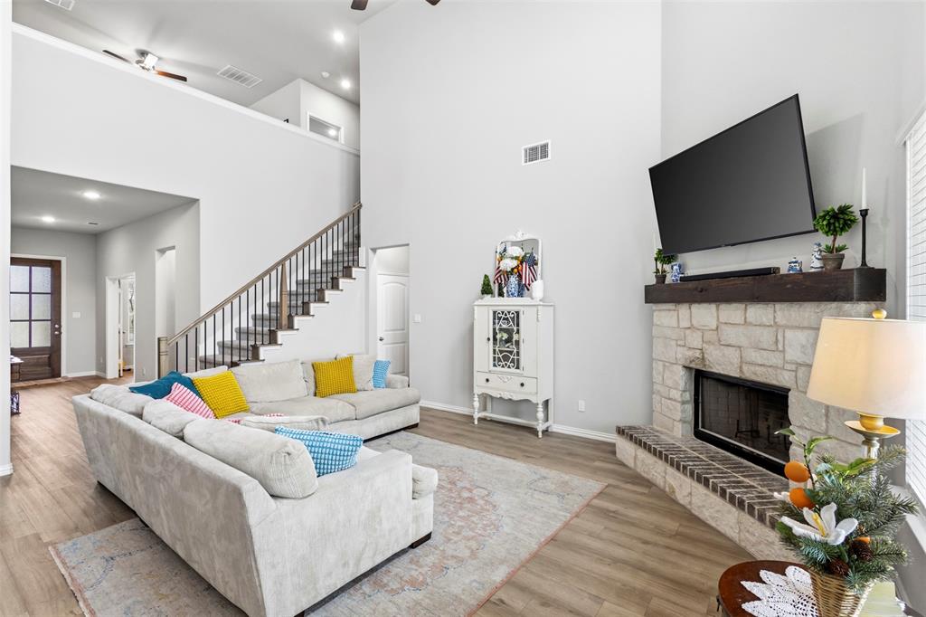 107 Yampa Court Rhome, TX 76078 - Photo 3 of 30 Living area featuring a stone fireplace with a dark wood mantel, high ceilings, wood-finish flooring, a contemporary staircase with dark balusters, and a visible second-story loft