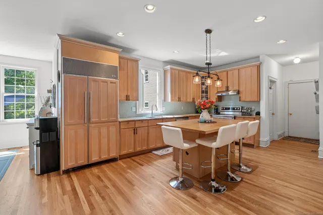 a kitchen with stainless steel appliances granite countertop a refrigerator a sink dishwasher a dining table and chairs with wooden floor