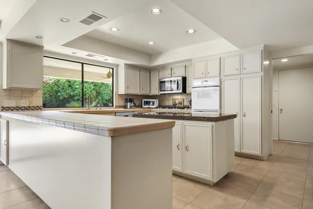 a kitchen with stainless steel appliances granite countertop a refrigerator a sink dishwasher a stove and white cabinets with wooden floor