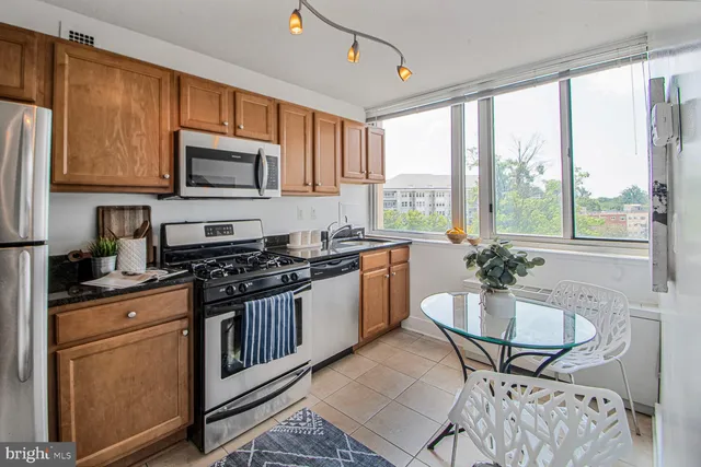 a kitchen with stainless steel appliances granite countertop a refrigerator a stove a sink a dining table and chairs