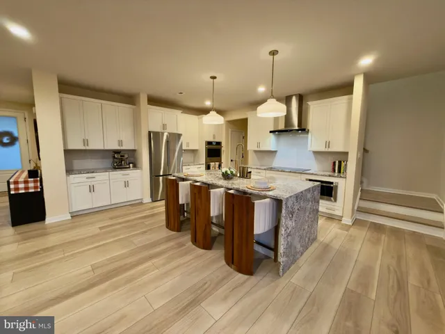 a large kitchen with stainless steel appliances kitchen island granite countertop a stove a refrigerator a sink dishwasher a dining table and chairs with wooden floor