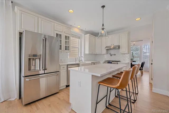 a kitchen with stainless steel appliances granite countertop a refrigerator a sink dishwasher a stove and white cabinets with wooden floor