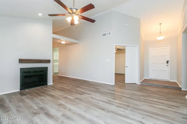 an empty room with wooden floor a ceiling fan a kitchen and a fireplace