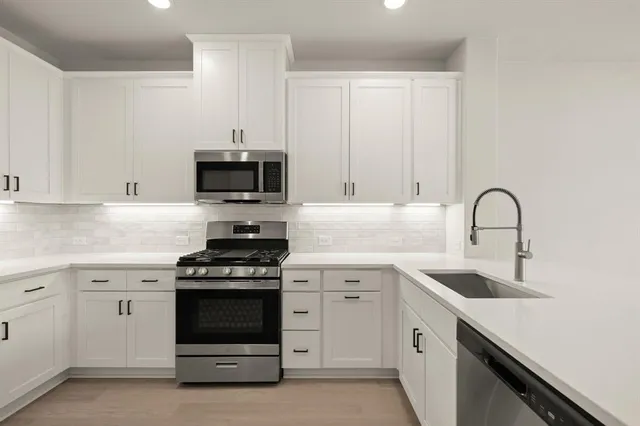 a kitchen with stainless steel appliances a sink a stove a refrigerator a white cabinets and wooden floor