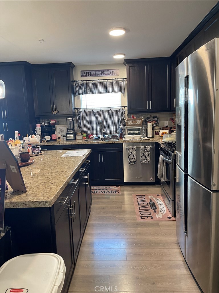 110 Main Street Piru, CA 93040 - Photo 5 of 15 a kitchen with stainless steel appliances granite countertop a refrigerator a stove a sink dishwasher and wooden cabinets with wooden floor