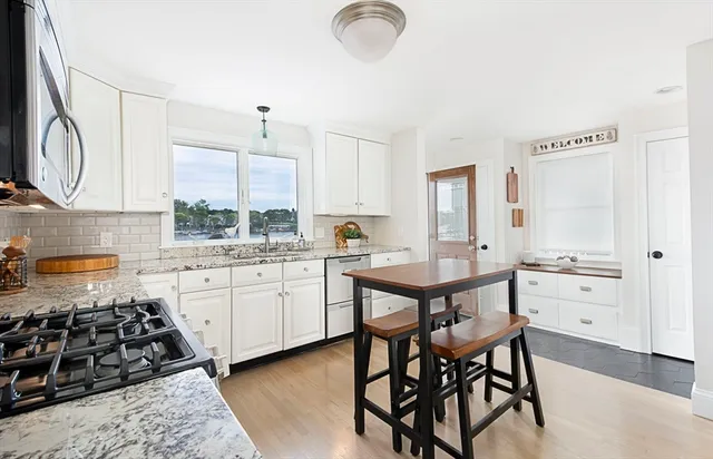 a kitchen with stainless steel appliances granite countertop a stove a sink dishwasher and white cabinets with wooden floor