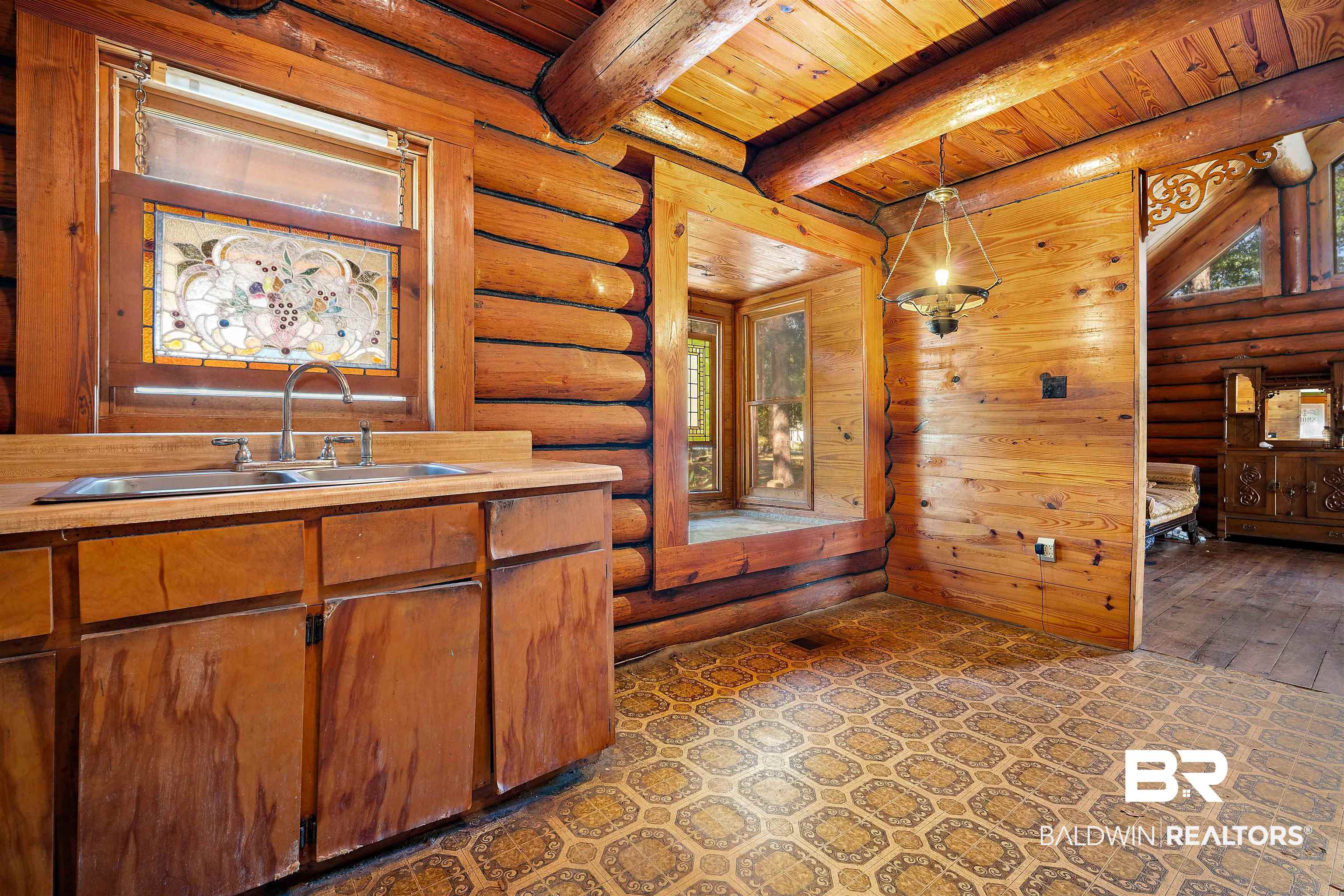 11236 Wren Avenue Fairhope, AL 36532 - Photo 13 of 35 Kitchen featuring log walls, a wood ceiling with exposed beams, light countertops, hanging light fixtures, and brown cabinets