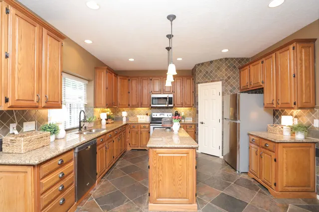 a kitchen with stainless steel appliances kitchen island granite countertop a refrigerator a sink dishwasher and a stove with wooden cabinets