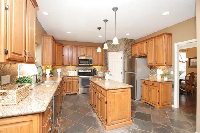 a kitchen with stainless steel appliances granite countertop a stove top oven a sink a refrigerator and white cabinets with wooden floor