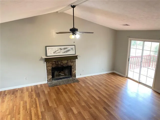 a view of an empty room with wooden floor fireplace and a window