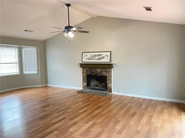 a view of an empty room with wooden floor fireplace and a window