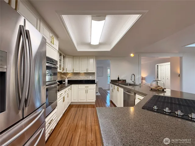 a kitchen with stainless steel appliances granite countertop a refrigerator a sink dishwasher a stove and white countertops with wooden floor