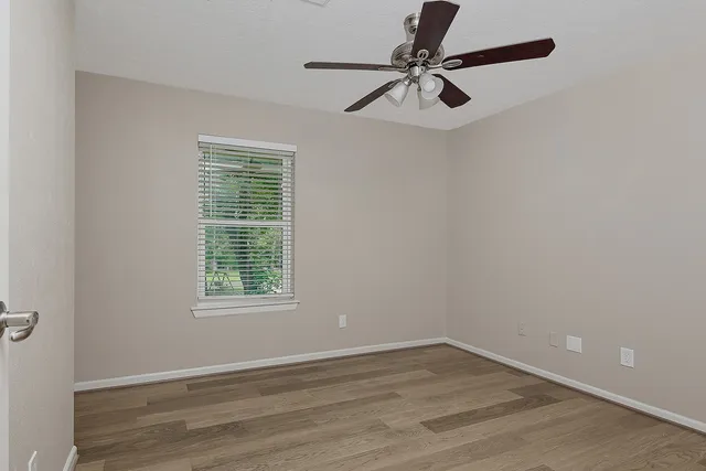 an empty room with wooden floor fan and windows