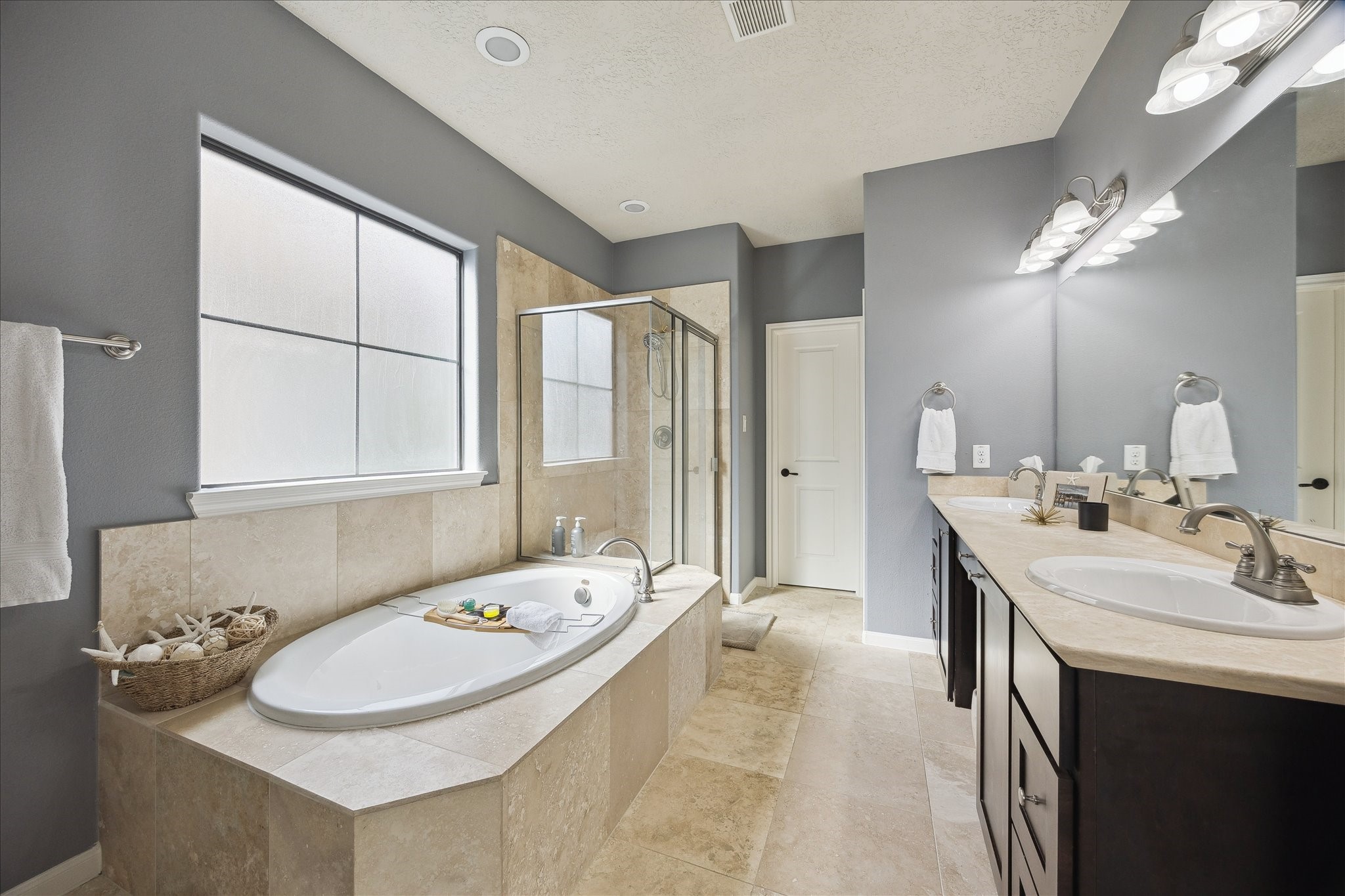 1110 West 25th Street Houston, TX 77008 - Photo 22 of 40 This spa-inspired primary bathroom is a true showpiece, offering a luxurious retreat within the home. Designed for relaxation, it features a soaking tub set into a tiled surround, a separate glass-enclosed shower, and an expansive double vanity with elegant countertops and modern fixtures. Soft natural light, soothing tones, and thoughtful lighting create a calm, resort-like atmosphere.