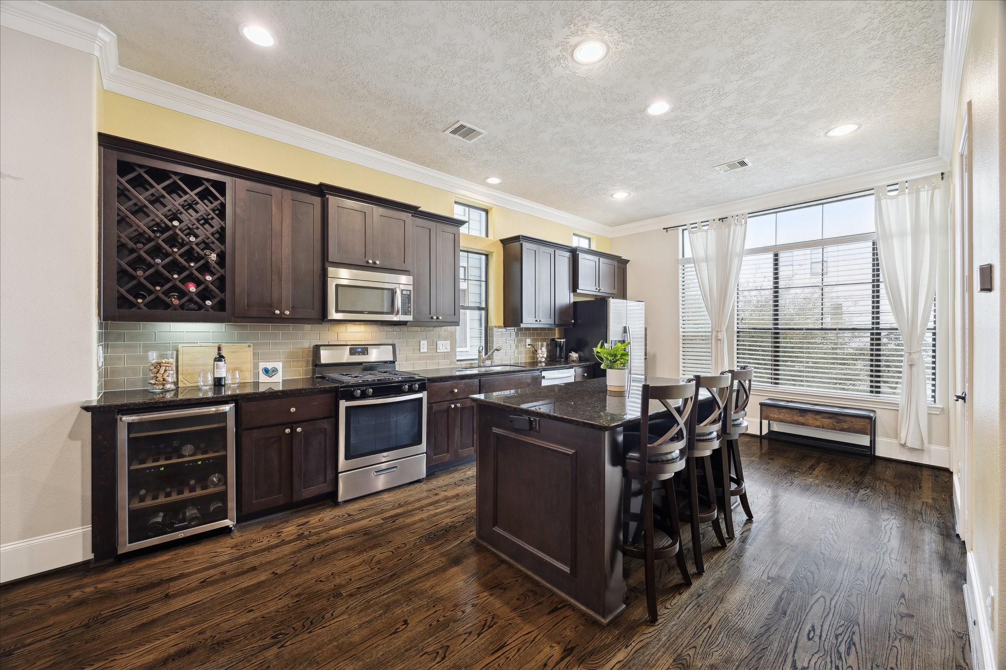 1110 West 25th Street Houston, TX 77008 - Photo 9 of 40 This stunning kitchen is the heart of the home, designed for both everyday living and effortless entertaining. Rich espresso cabinetry, gleaming granite countertops, and stainless steel appliances create a sophisticated yet inviting aesthetic, while the oversized island offers generous seating and prep space. A built-in wine fridge and dedicated wine storage add a touch of luxury, perfect for hosting friends or enjoying quiet evenings in.