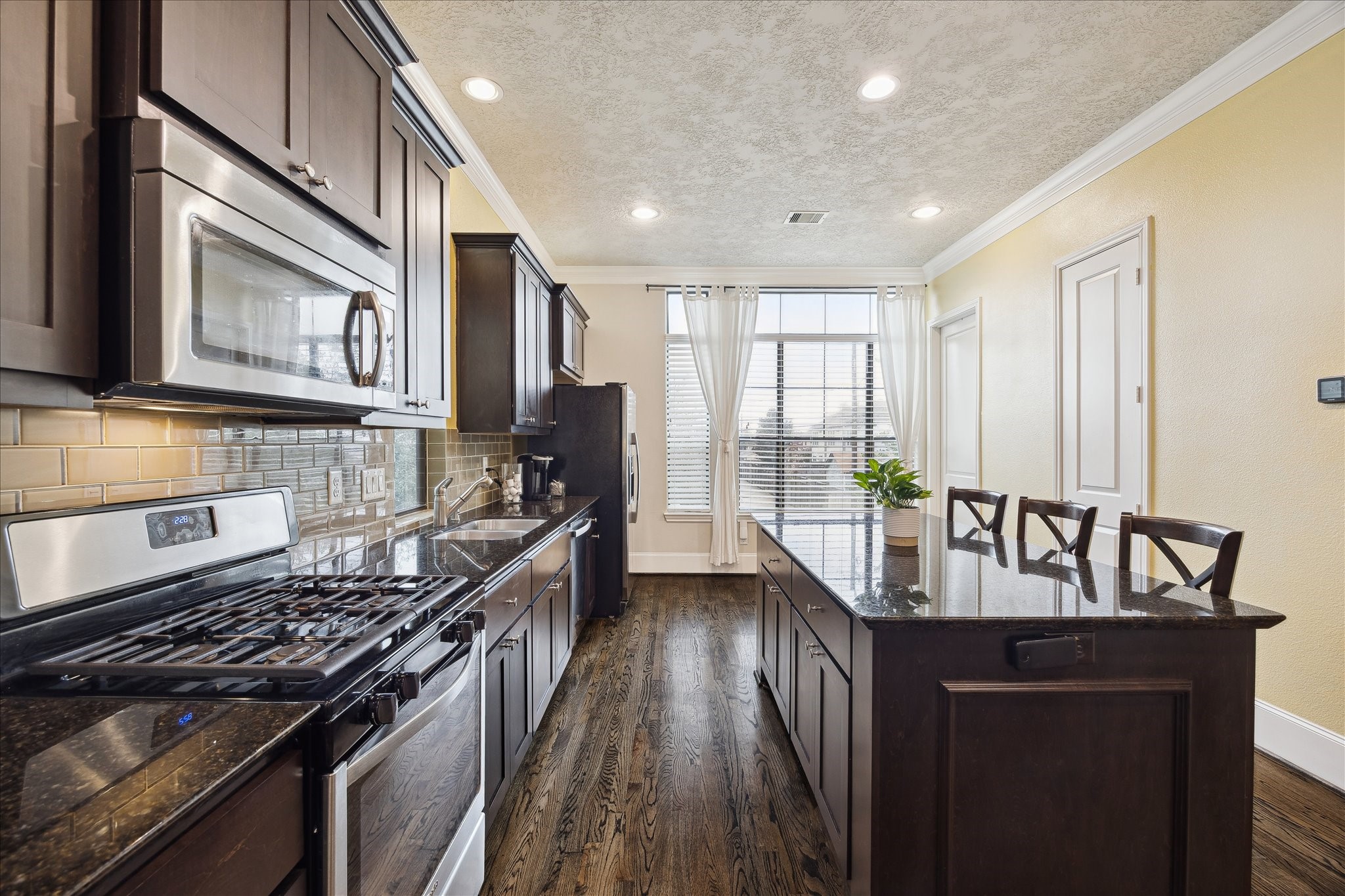 1110 West 25th Street Houston, TX 77008 - Photo 10 of 40 The expansive island provides ample seating and prep space, ideal for casual meals, morning coffee, or entertaining guests. Bathed in natural light from large windows and finished with warm hardwood floors and recessed lighting, this kitchen feels open, polished, and effortlessly livable—an inviting space where one can easily picture gathering, cooking, and making memories.