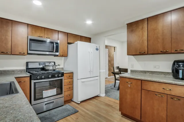 a kitchen with granite countertop wooden cabinets a stove a microwave a refrigerator a sink and dishwasher with wooden floor