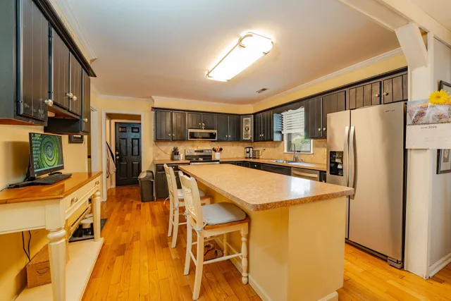 a kitchen with stainless steel appliances granite countertop a refrigerator a stove top oven a sink dishwasher and white cabinets with wooden floor